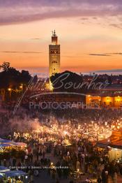 Image du Maroc Professionnelle de  Au coucher du soleil et même un peu avant la foule envahi la fameuse Place Jemaa El Fana qui se métamorphose en un gigantesque restaurant en plein air grâce aux nombreux stands et gargotes qui s'y installent sur ce lieu mythique au centre de la médina de Marrakech. Au fond le minaret de la Koutoubia, Samedi 26 Février 2005. (Photo / Abdeljalil Bounhar)

